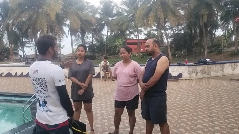 Instructor in a white top talks three students through the plan beside the pool