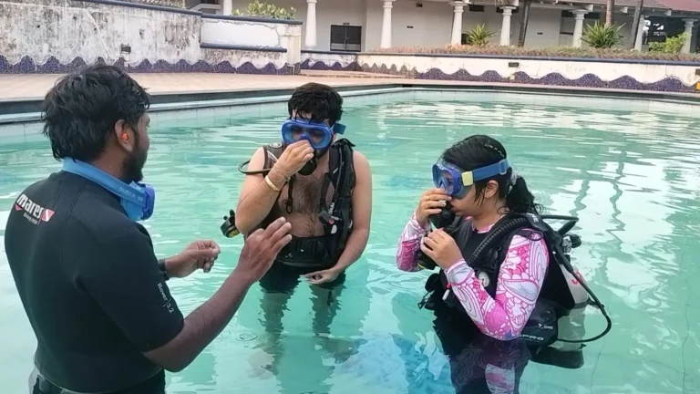 Instructor in a wetsuit explains mask clearing to two students standing in a resort pool