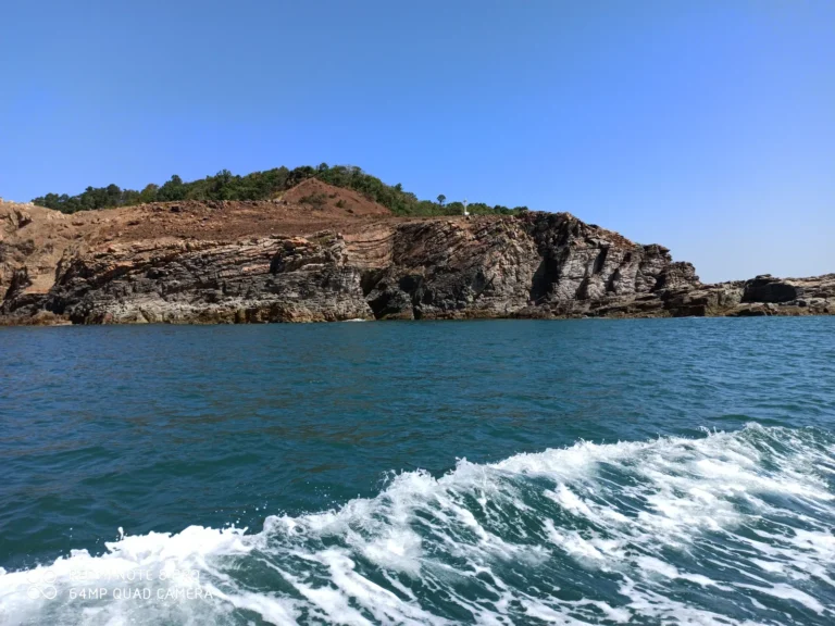 Boat wake curling in front of a rocky island with layered cliffs and green scrub on top