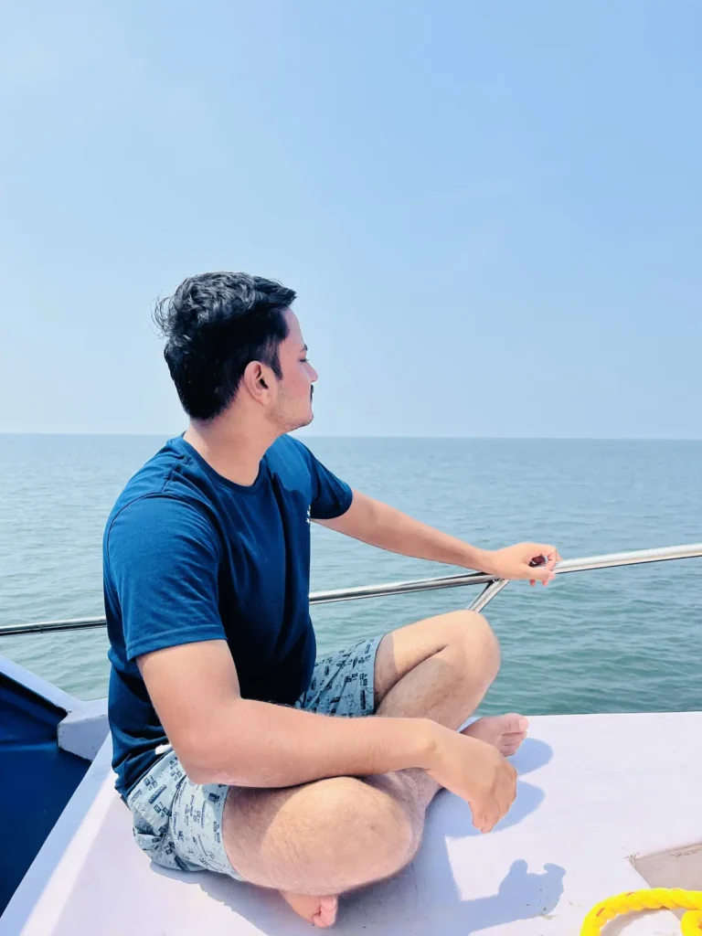 A man sits cross-legged on the front deck of a boat, gazing out at the open sea