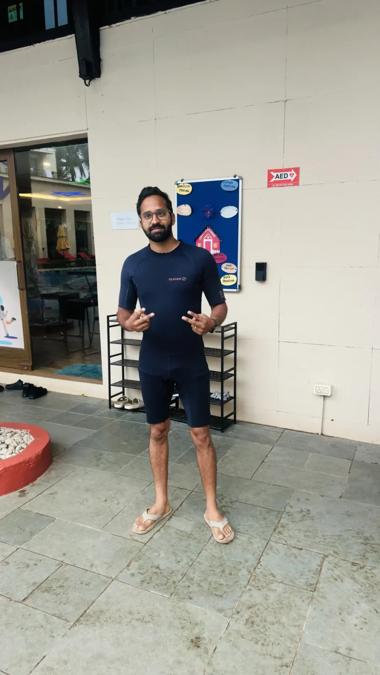 A man in a wetsuit talks with his hands raised, standing on the tiled floor outside the dive centre