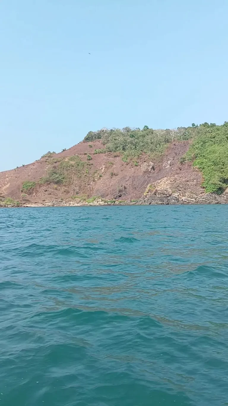Calm blue sea in front of a red rocky headland topped with green scrub under a clear sky