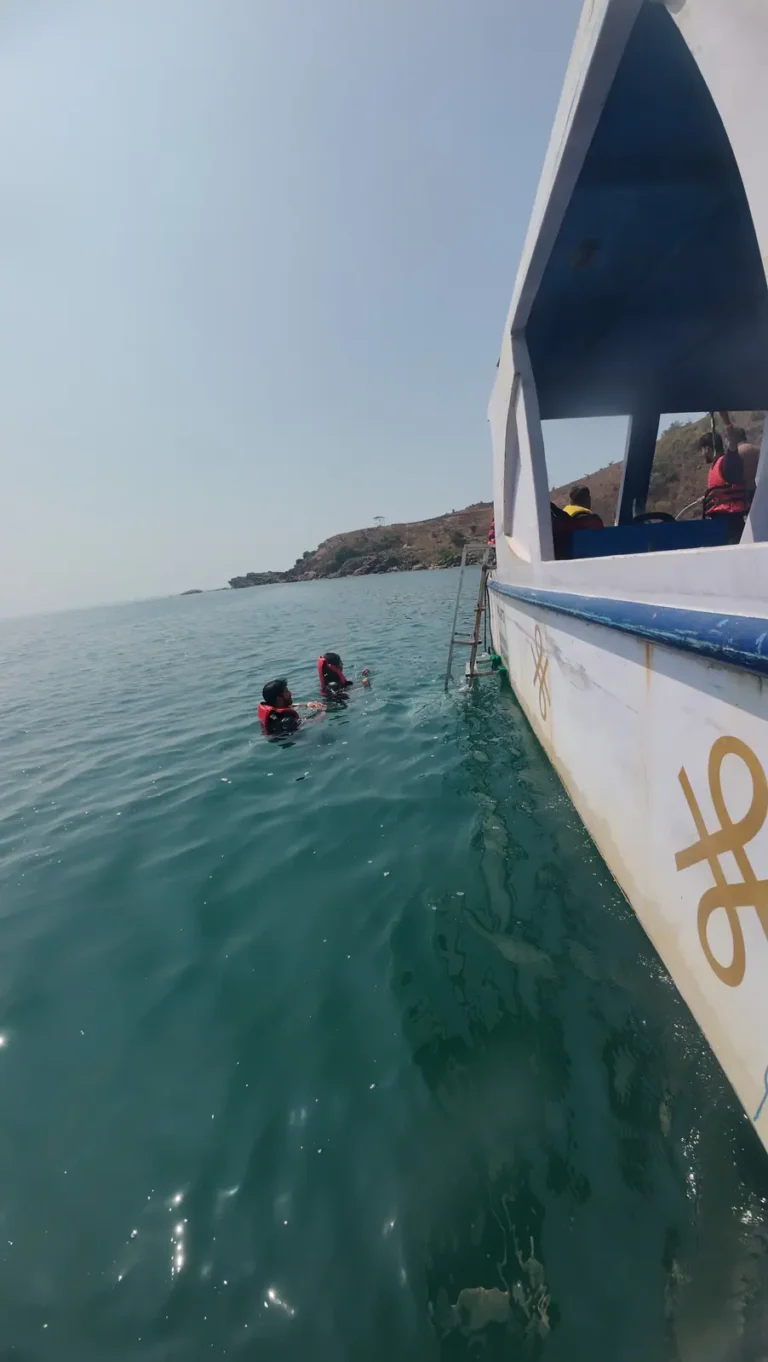 Two snorkelers float beside the white hull of a dive boat, with a headland on the horizon