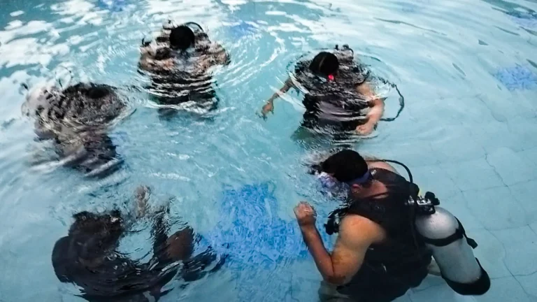 Students with their heads underwater practise skills in a pool while a geared up instructor watches closely