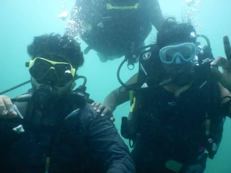 Three divers huddle together for a photo in clear blue-green water, one making a hand sign