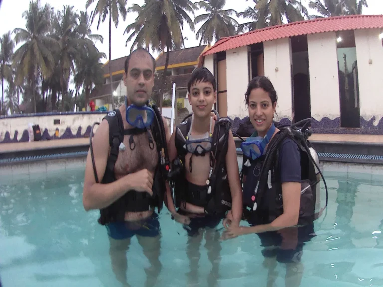Man, boy and woman stand in the resort pool wearing BCDs and masks, ready for training