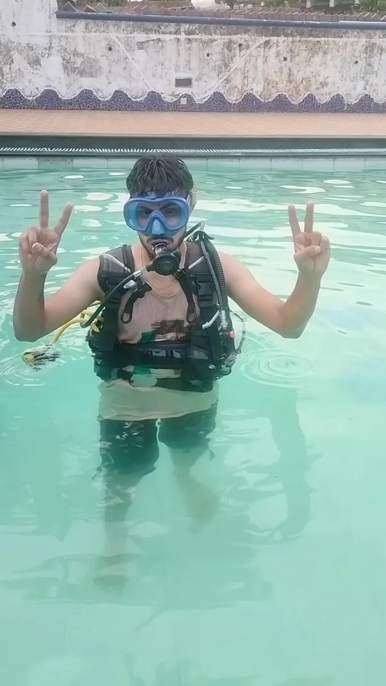 Young man in a mask and BCD stands in the pool making peace signs with both hands